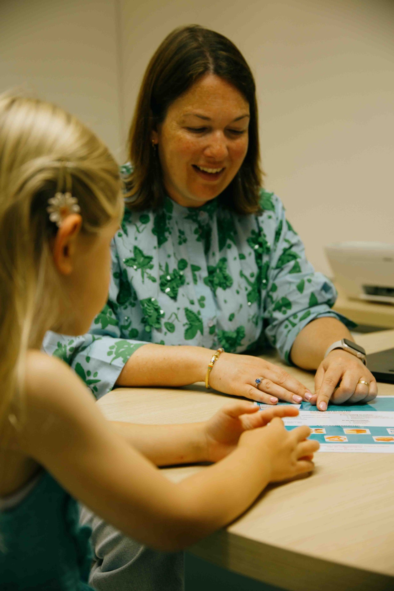 Kinderdiëtist zit aan een tafel en geeft uitleg aan een kind